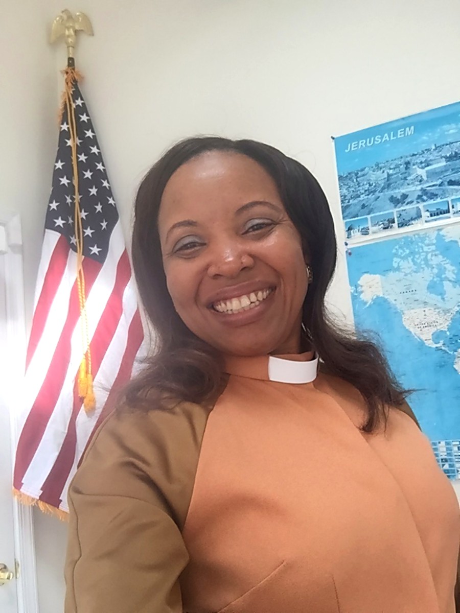 Pastor Joyce Ojiaku smiling beside the American flag